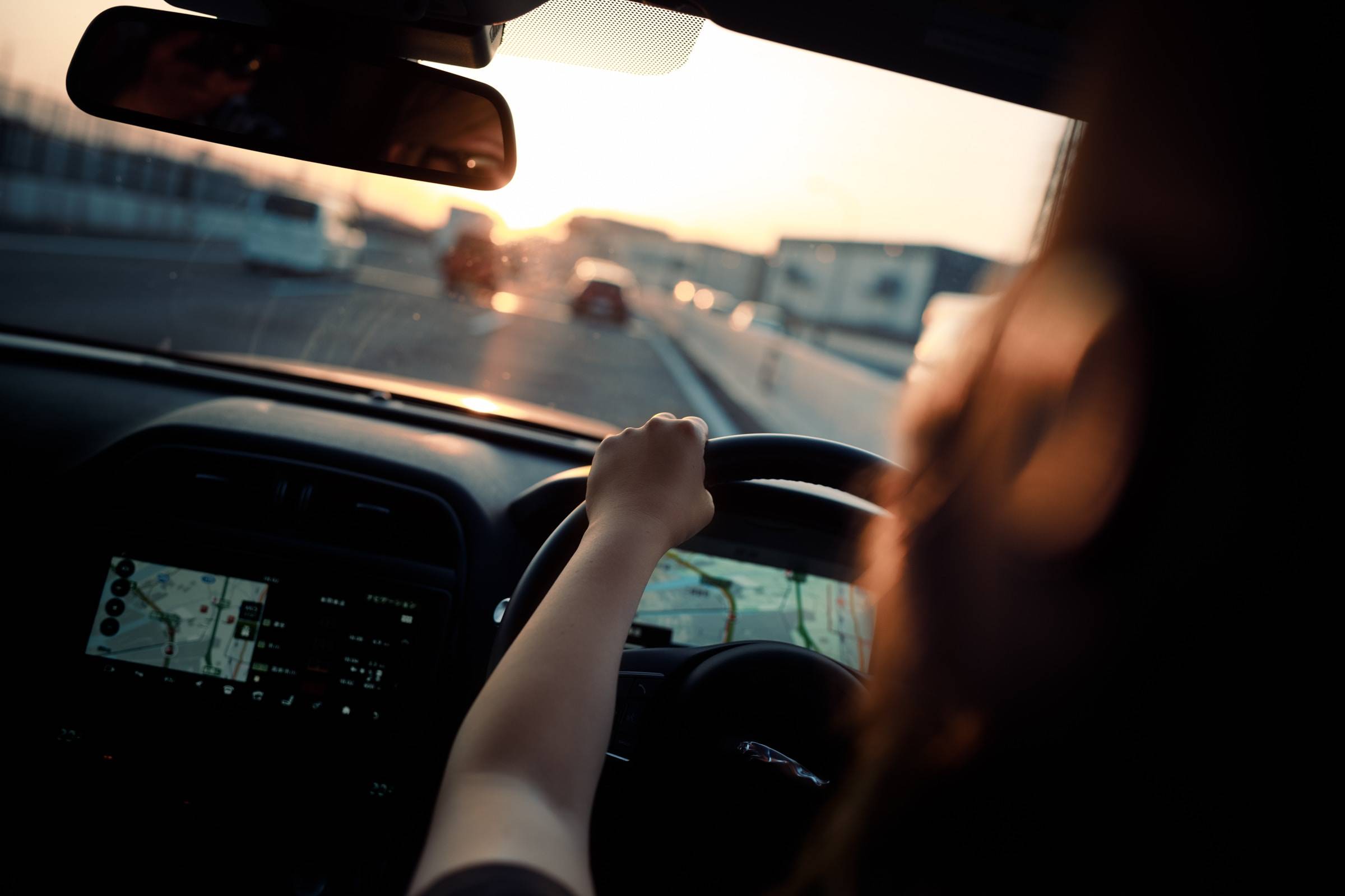 A woman driving a car at sunset.